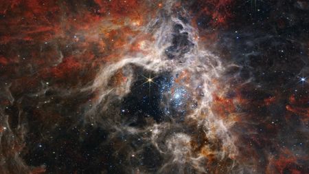 A photo of a nebula with swirling cream and orange clouds, and blue-tinted stars in the middle
